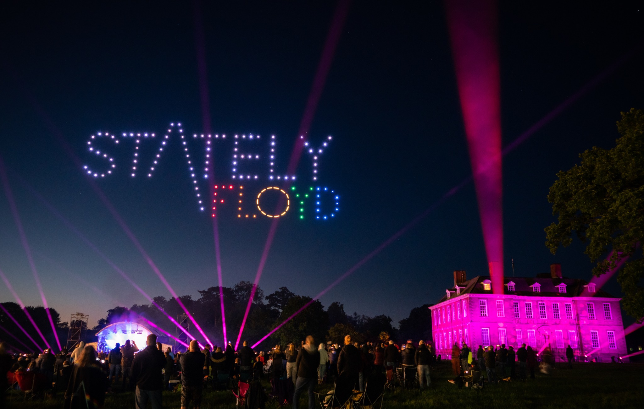 Large festival audience watching a drone display and event lighting
