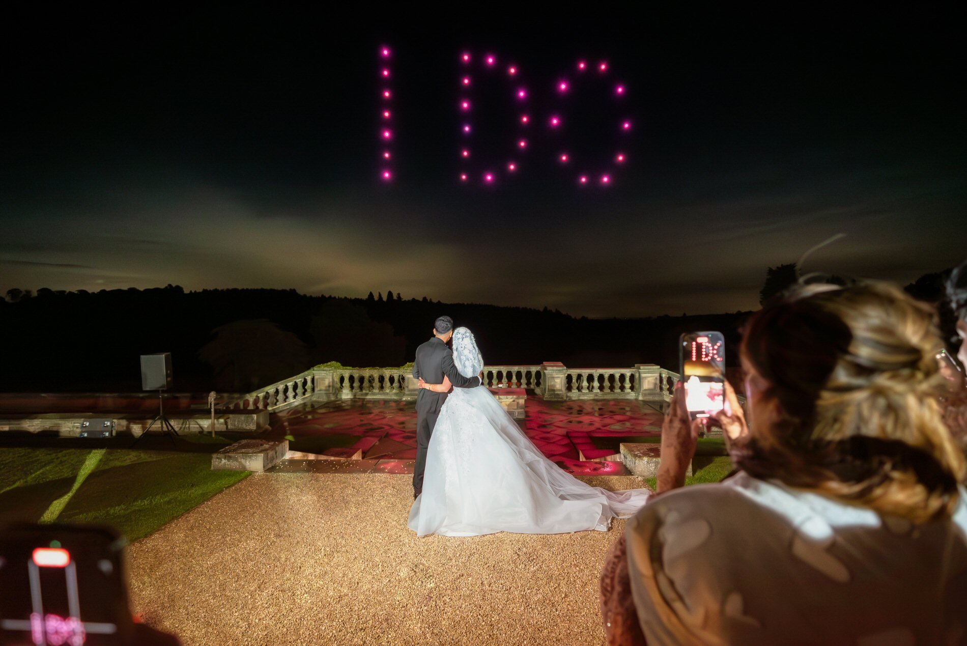 Bride and groom beneath I DO written in illuminated drones