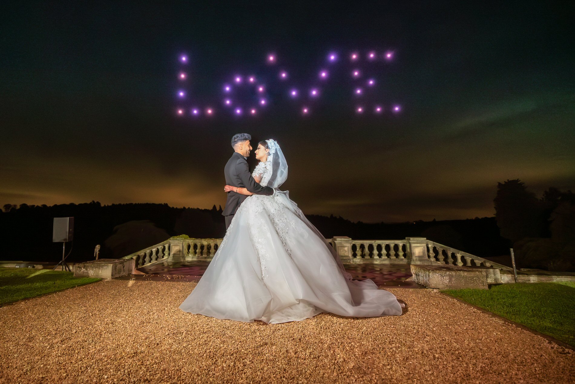Newlywed couple beneath the word LOVE formed by illuminated drones