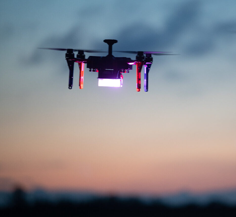 A drone from a dazzling light show flies against a dusky sky with a blurred background.