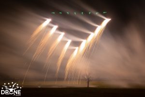 The drone show in the sky created bright cascading patterns with a tree in the foreground.