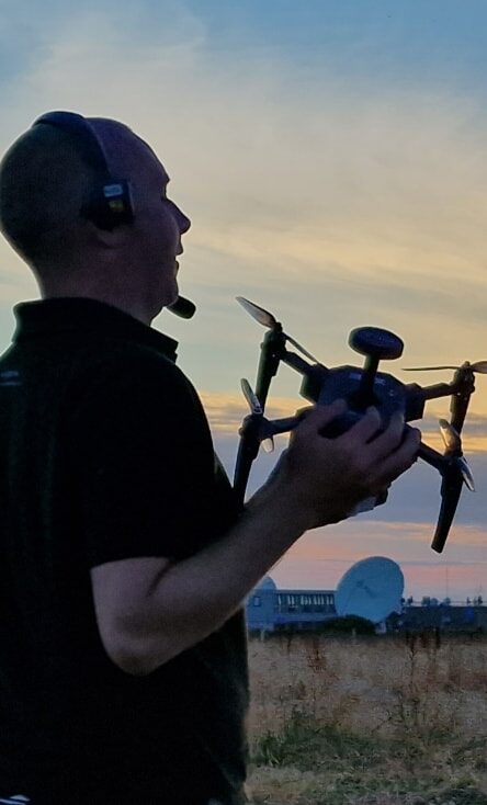 Man holding a drone and wearing a headset, standing in a field during sunset, preparing for an awe-inspiring drone light show.