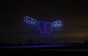 A nighttime drone light show forms the shape of a stylized buffalo with blue and purple lights in the sky.