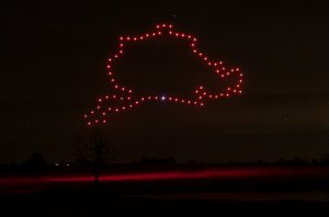 Red drones perform a stunning drone light show, forming the shape of Ukraine's map in the night sky with a dark landscape below.