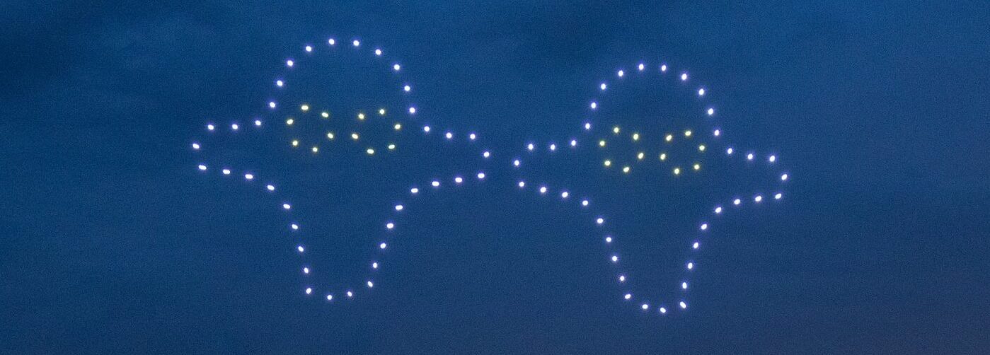 Two drone formations in a night sky create the outlines of two UFOs, each with small yellow lights in the center, forming a mesmerizing drone light show.