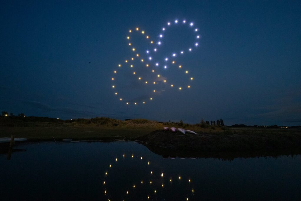 Drones create glowing patterns in the night sky, reflected in the water below.