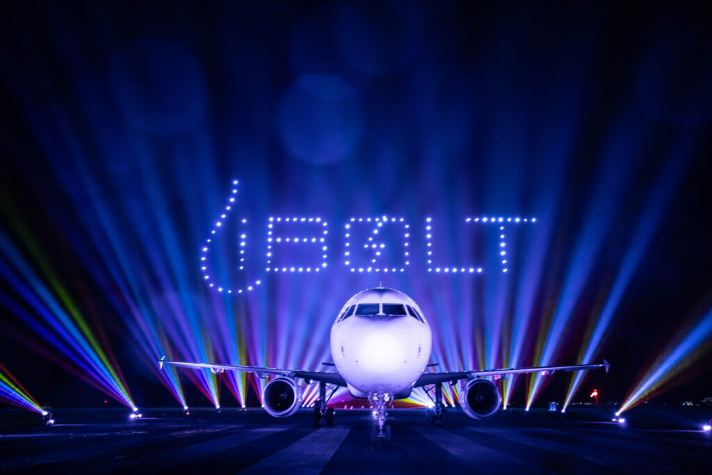 A plane on a runway at night with "BOLT" spelled out in lights and colorful beams in the background.