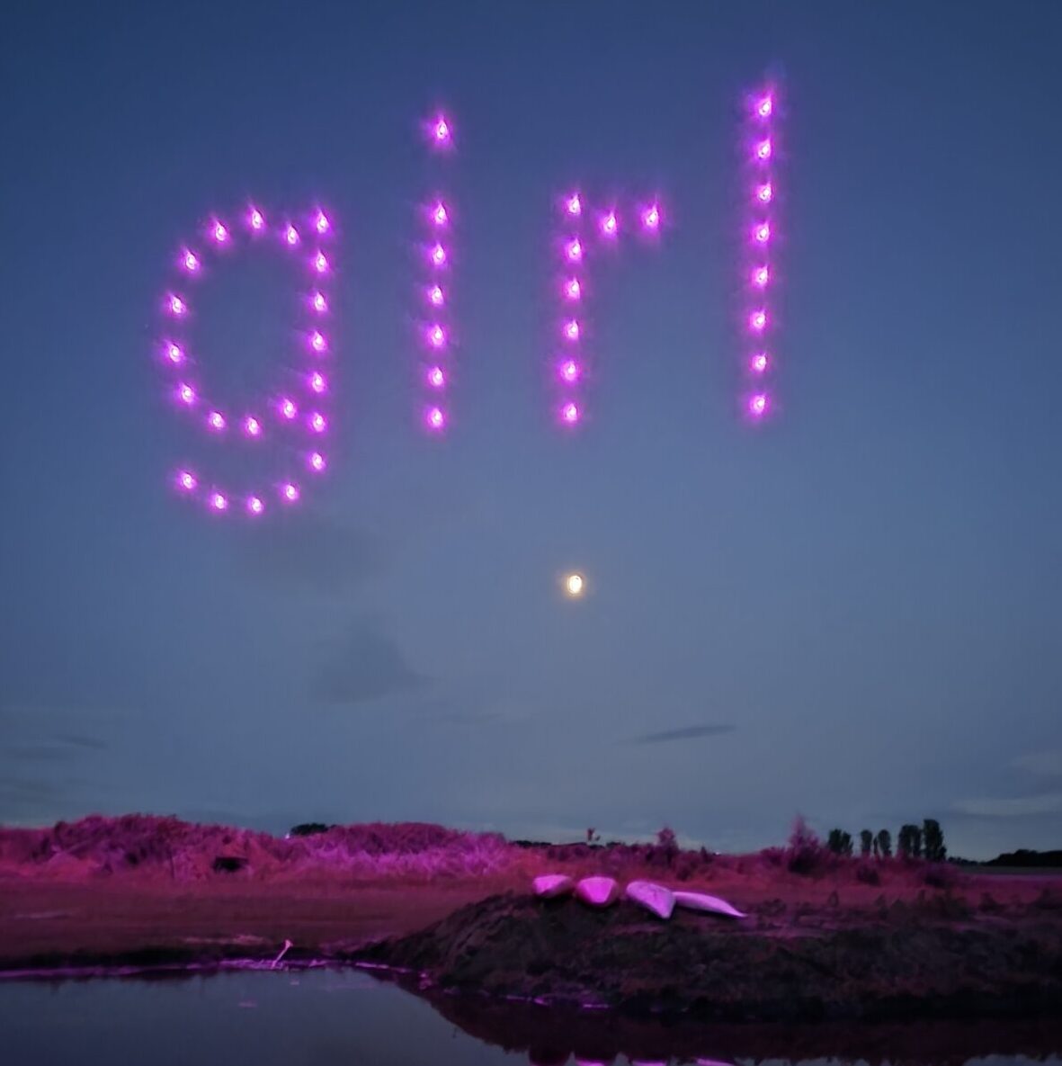 Pink drones in the night sky spell out "girl" above a moonlit landscape with shimmering water and grass. Sorry, there are no relevant SEO keywords in the provided description.